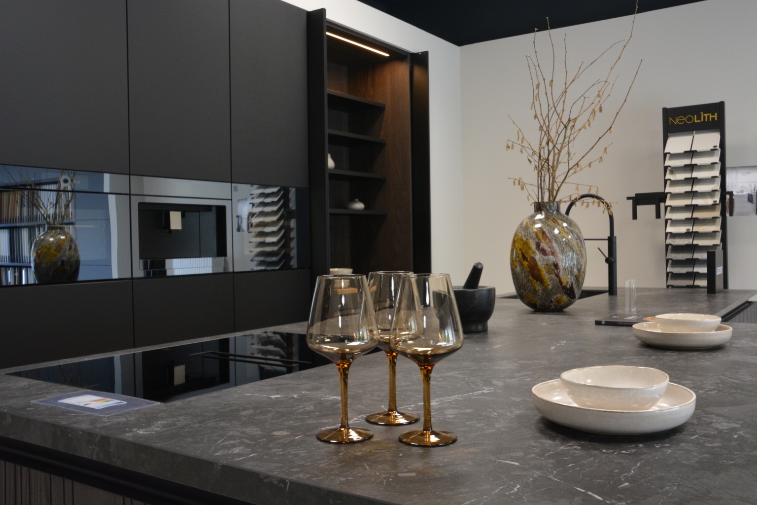 Kücheninsel mit drei Weingläsern und Geschirr vor Küchenzeile schwarz dunkel