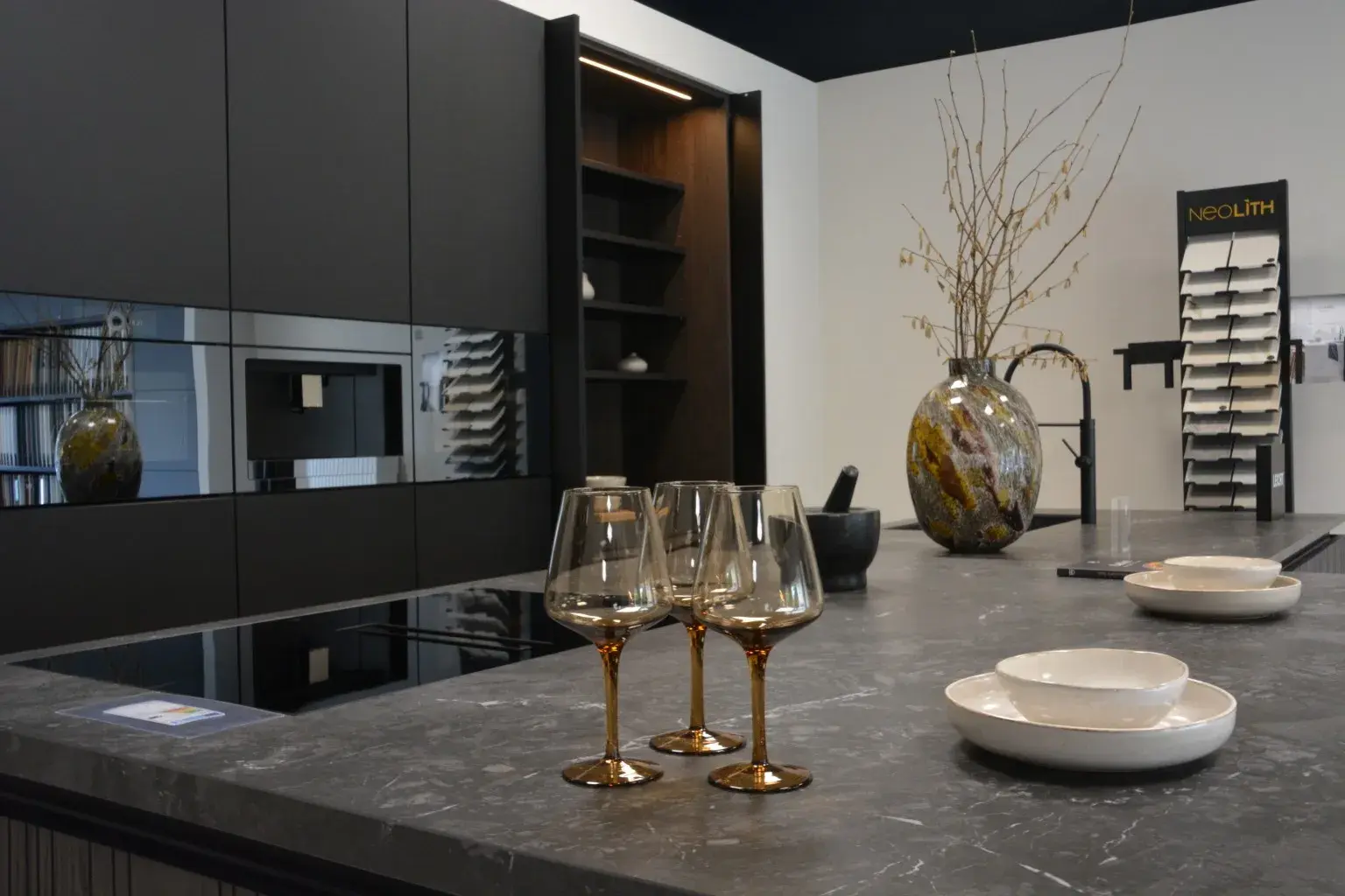 Kücheninsel mit drei Weingläsern und Geschirr vor Küchenzeile schwarz dunkel